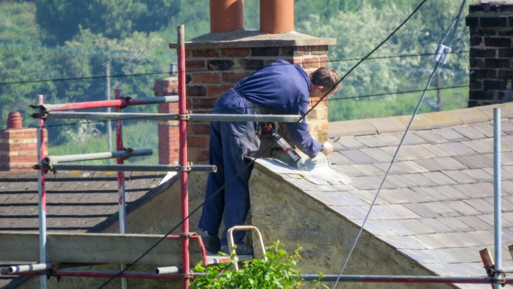 Roofer repairing chimney on slate roof in rural setting