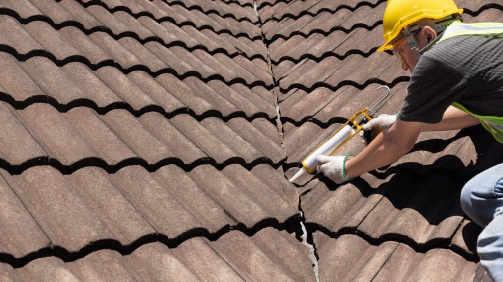 Worker man using silicone sealant adhesive to fix crack of the old tile roof