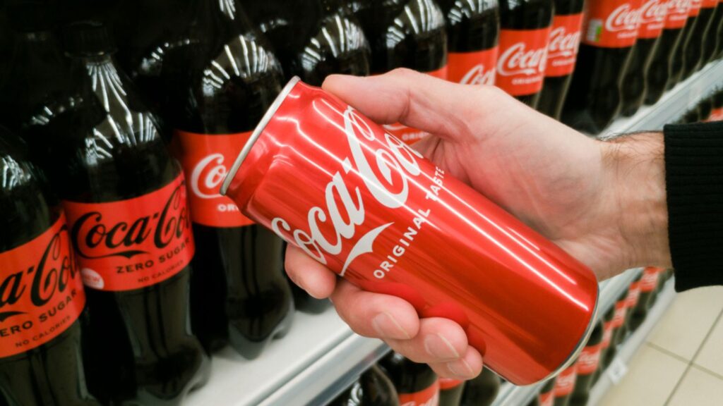 Zaporizhzhia, Ukraine - May 23, 2022 A red can of Coca-Cola in a man's hand against the background of a counter with bottles of Coca-Cola