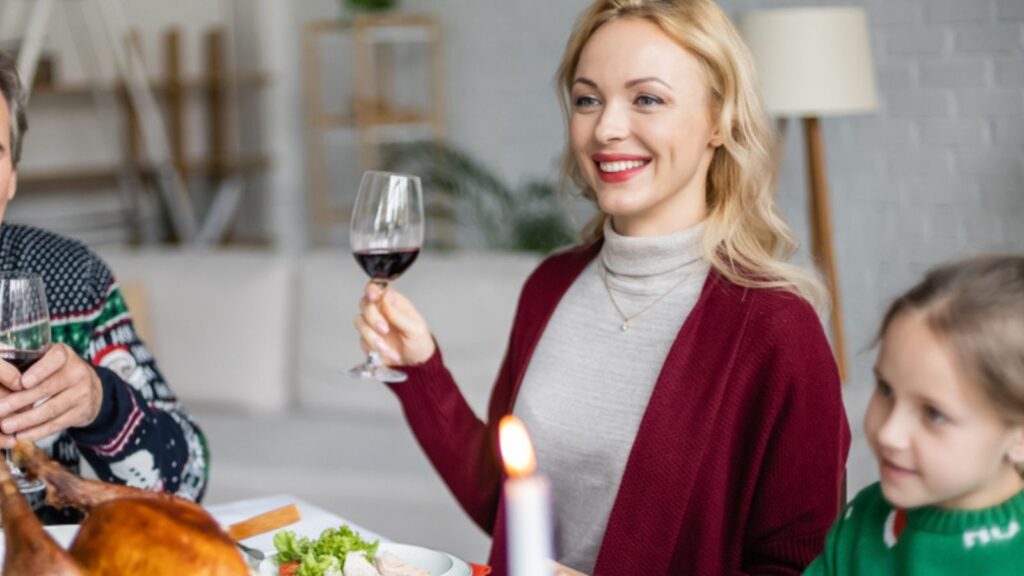 Cheerful woman toasting with glass of red wine near family and delicious thanksgiving dinner