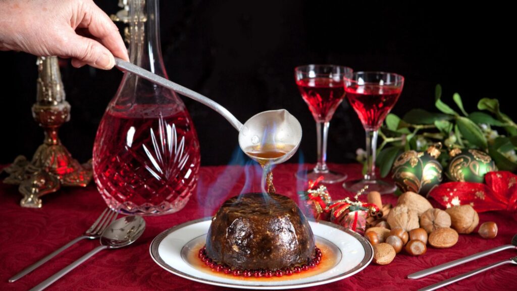 Christmas pudding flambe. Hand serving burning brandy over a christmas or plum pudding