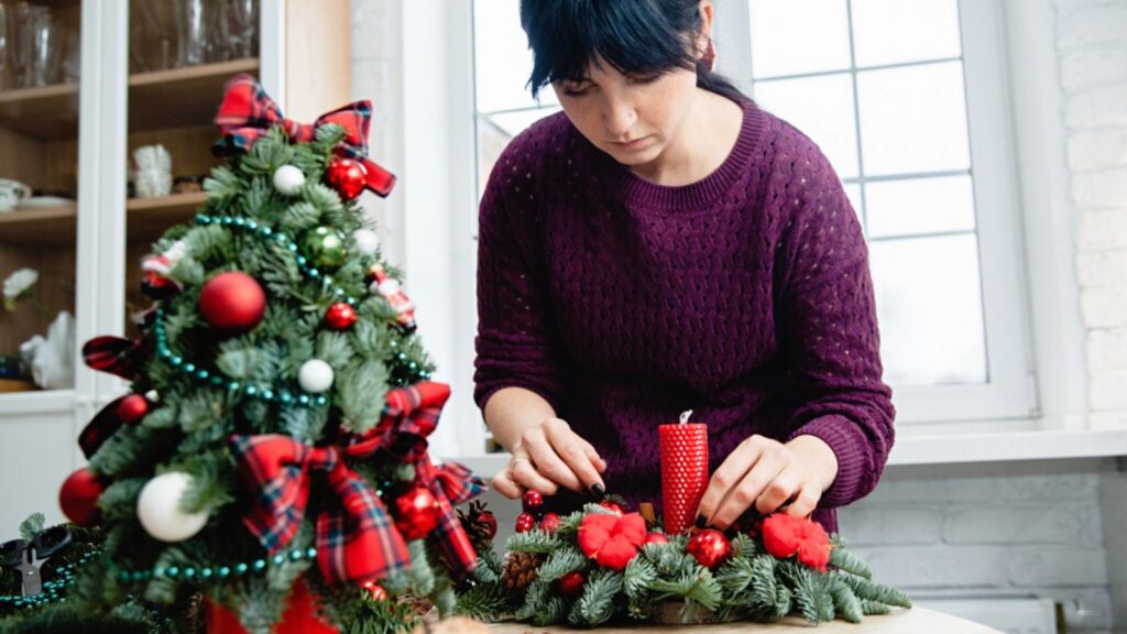 Decorator makes a Christmas decoration from spruce branches and red candle in the workshop.