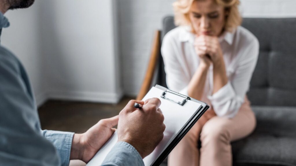 Depressed woman having psychologist therapy session at office while therapist writing in clipboard
