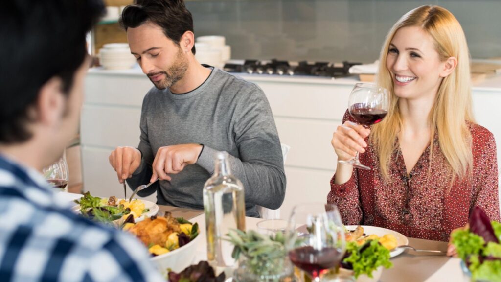 Happy young woman drinking a glass of red wine while talking to a friend at the party