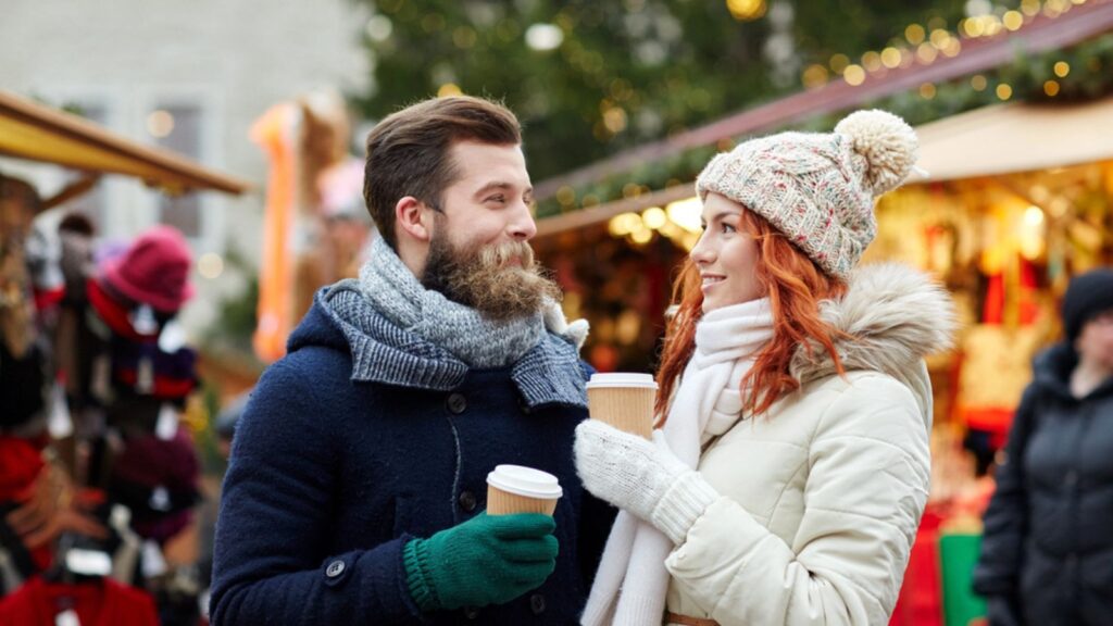 Holidays, winter, christmas, tourism and people concept- Happy couple drinking coffee on old town street