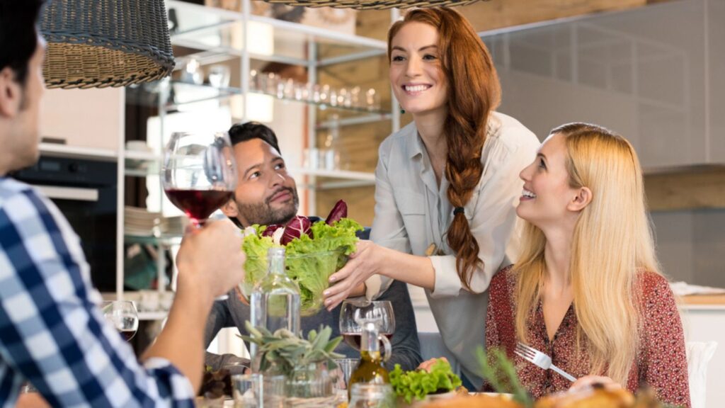 Host woman serving salad to guests at home. Smiling woman serving salad