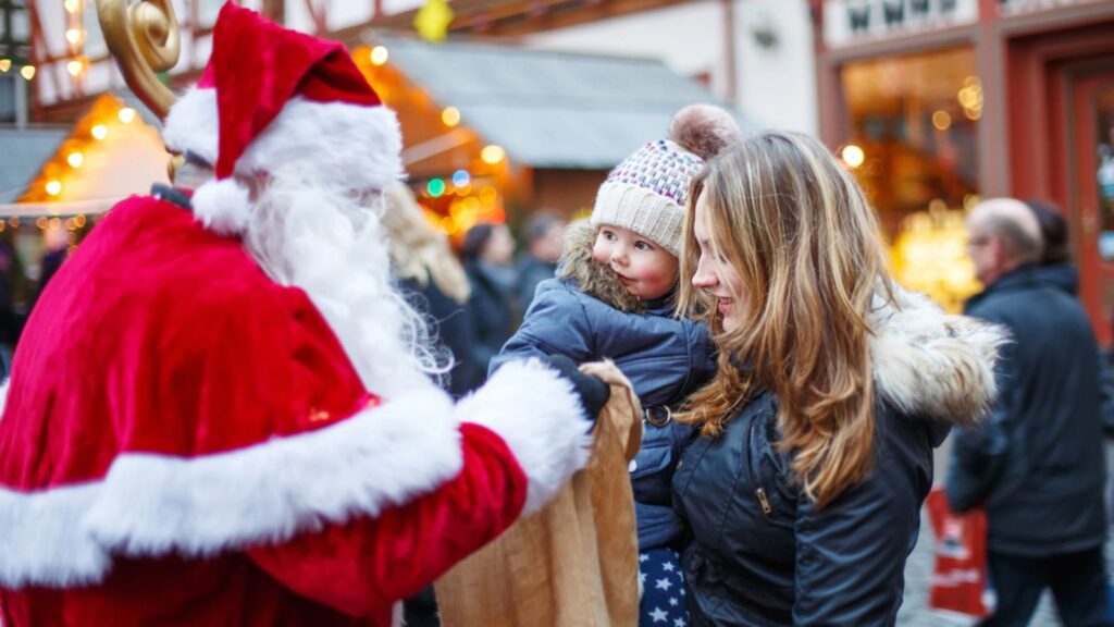 Little toddler girl with mother on Christmas market. Funny happy kid taking gift from Santa Claus.