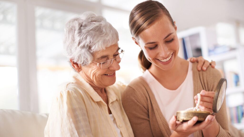 Mother, adult daughter and pearl necklace gift, special event or birthday with family heirloom for love and bonding in lounge. Women at home, happy giving jewelry as present and gratitude