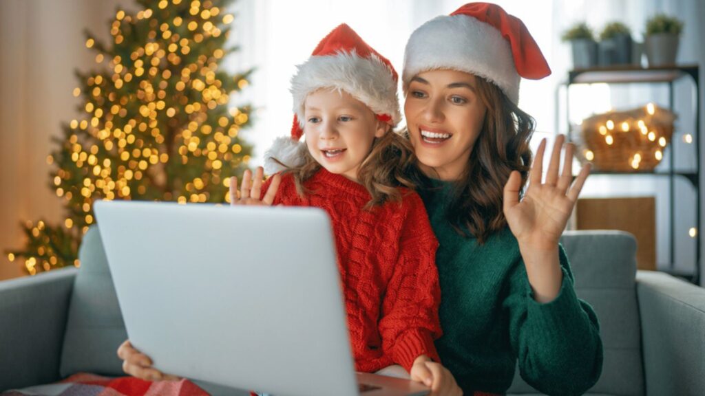 Mother and daughter are chatting with somebody using laptop in the living room decorated for Christmas.