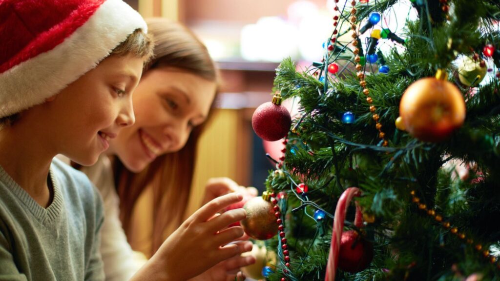 Portrait of happy boy in Santa cap decorating Christmas tree