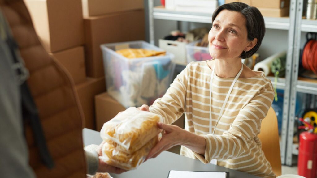 Portrait of smiling young woman volunteering at refugee help center and giving out food to people in need