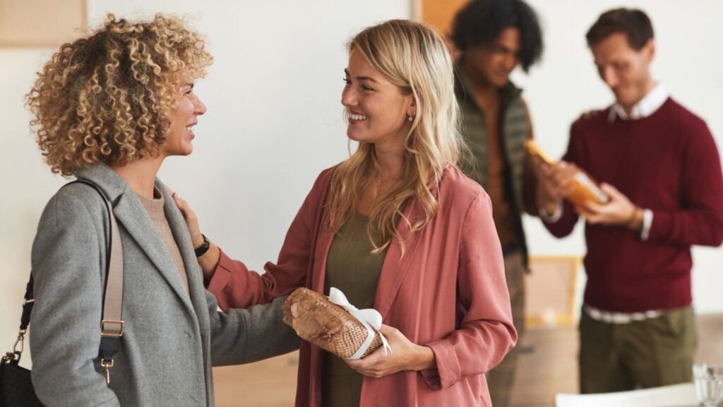 Side view at group of elegant adult people greeting each other and exchanging gifts while welcoming guests at dinner party indoors
