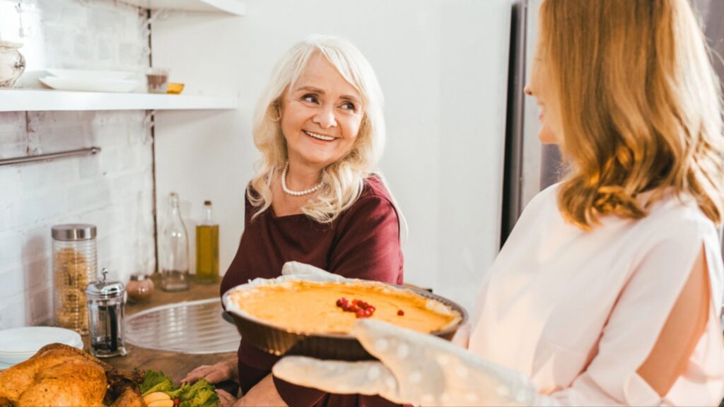 Smiling senior mother and daughter baking pumpkin pie together at home