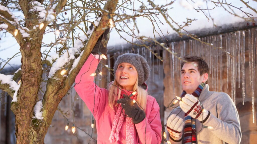 Two teenagers hanging fairy lightsin tree with icicles in foreground
