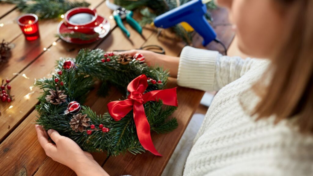 Winter holidays, diy and hobby concept - close up of woman holding handmade fir christmas wreath at home