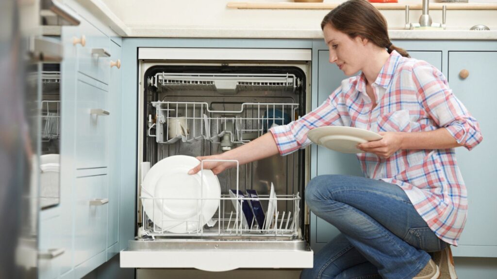 Woman Loading plates Dishwasher In Kitchen