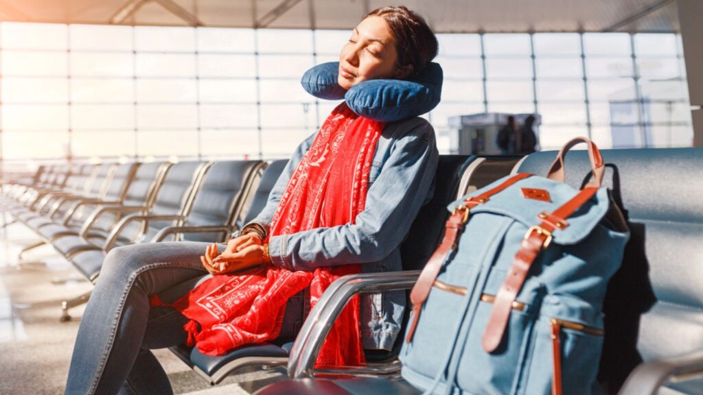 Woman relaxing and sleeping with neck pillow at airport terminal awaiting the delayed flight, transportation and travel concept