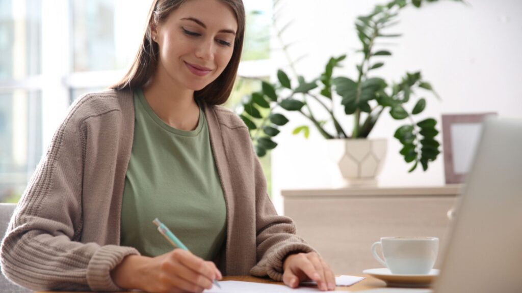 Woman writing letter at wooden table in room