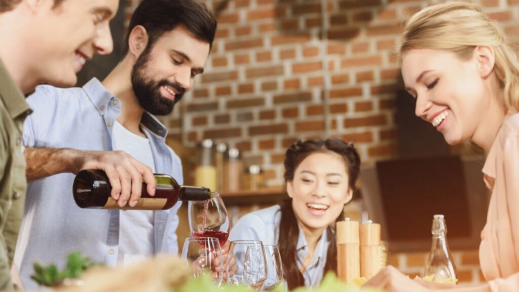 Young people partying at kitchen, eating and drinking wine at home party