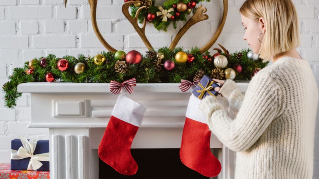 Young woman putting gift in christmas stocking at fireplace
