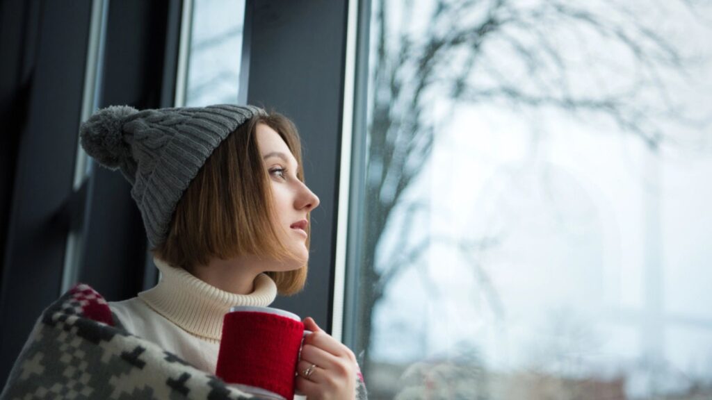 Girl holding red cup of tea and looking at the window