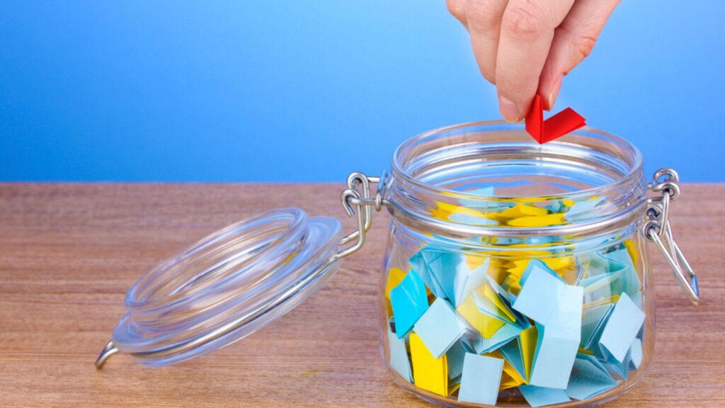 Hand throwing piece of paper for lottery on wooden table on blue background