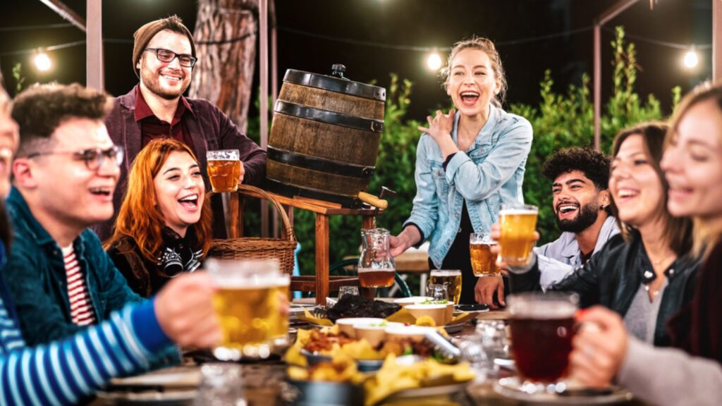 Happy men and women having fun drinking out at beer garden - Social gathering life style concept enjoying hangout time together at night