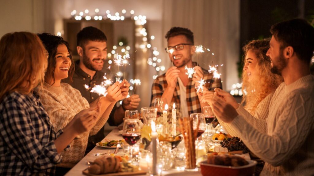 Holidays, celebration, and people concept- happy friends with sparklers having christmas dinner at home.