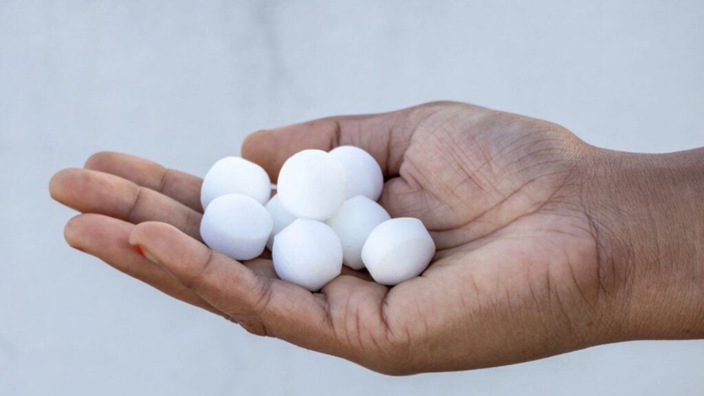 Many white naphthalene balls on a female hand. They are also known as mothballs