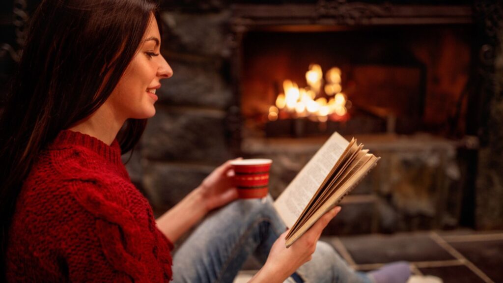 Smiling young girl reading book in front of fireplace